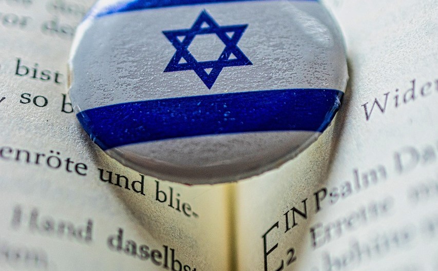 An open bible scripture with a button on top of an Israel emblem on it